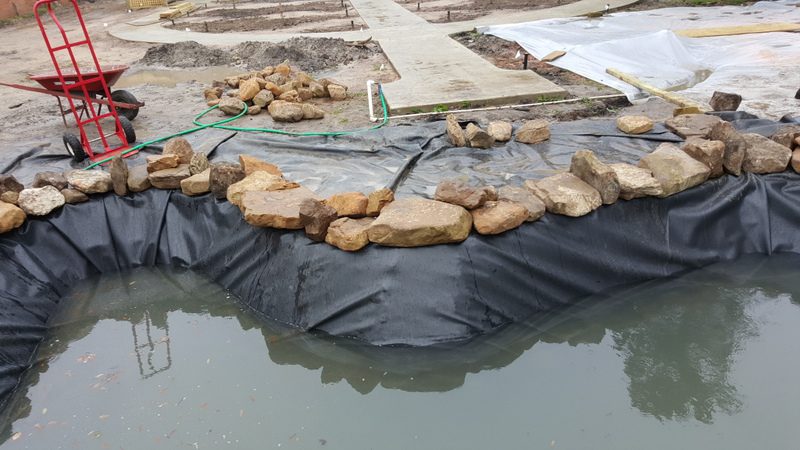 A pond with rocks in the water and tarps.