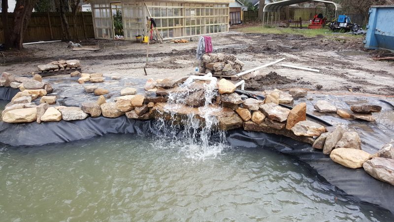 A pond with water flowing from it and rocks around.