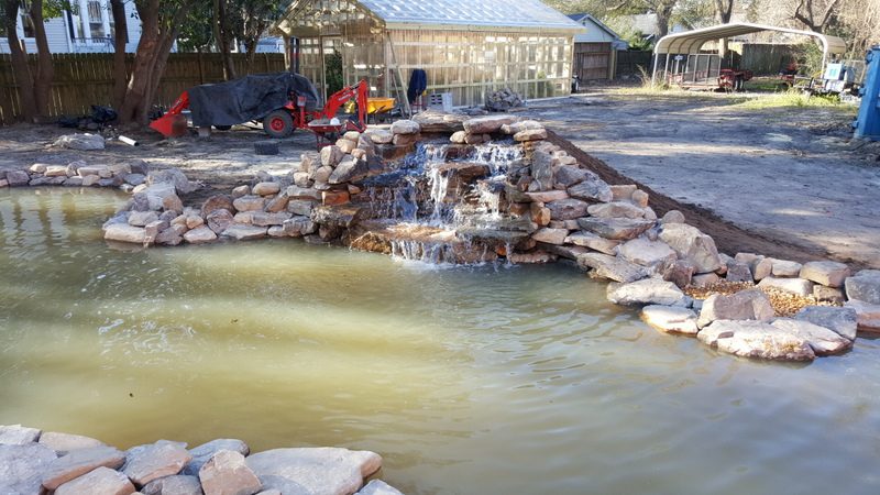 A pond with water flowing over it and rocks around.