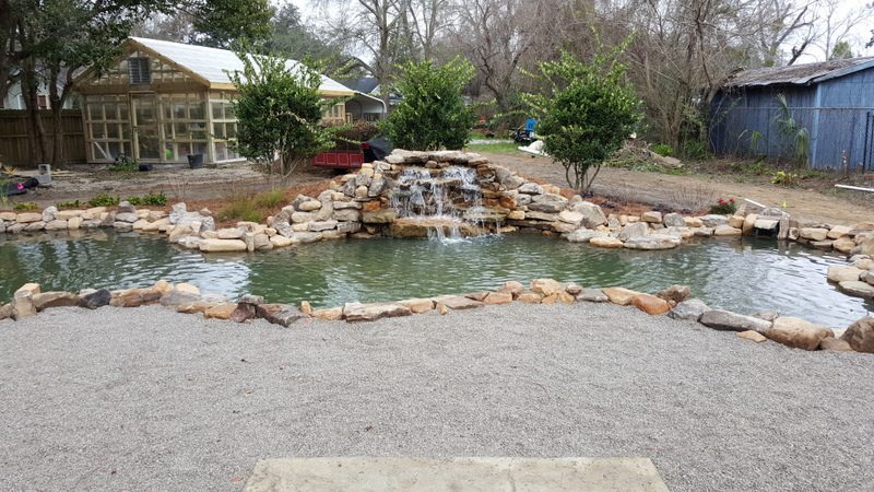 A pond with water flowing over it and rocks around.