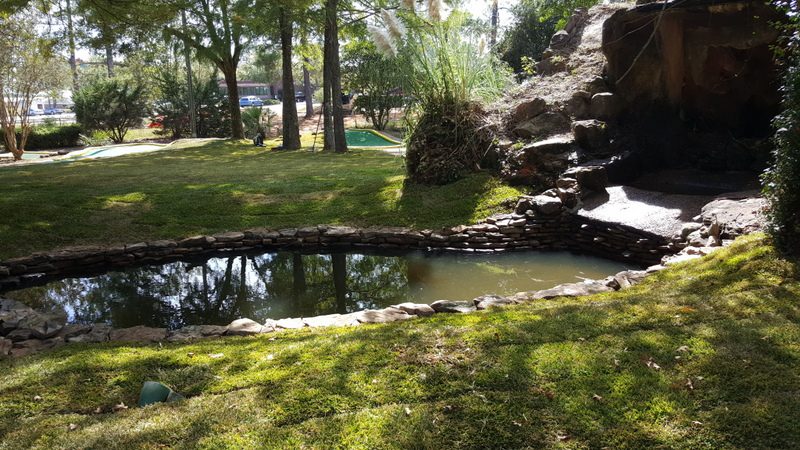 A pond with water running down it and rocks in the ground.