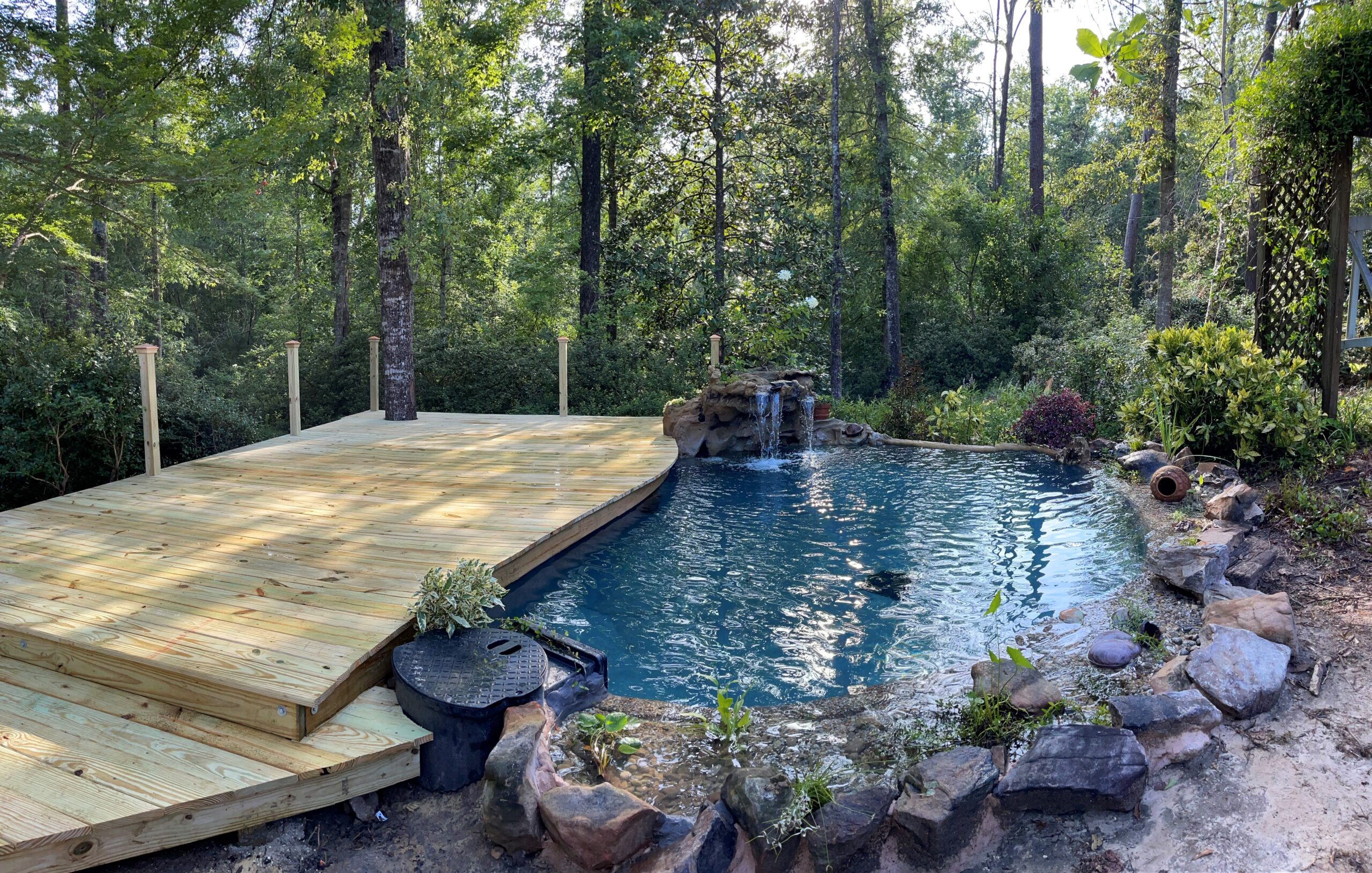 A pool with a wooden deck and waterfall.