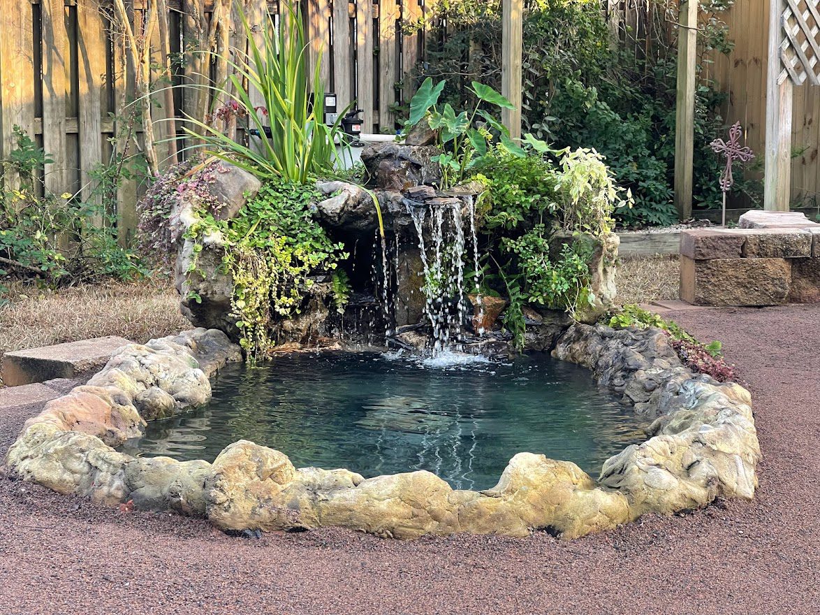 A pond with water flowing over it and plants growing on the side.