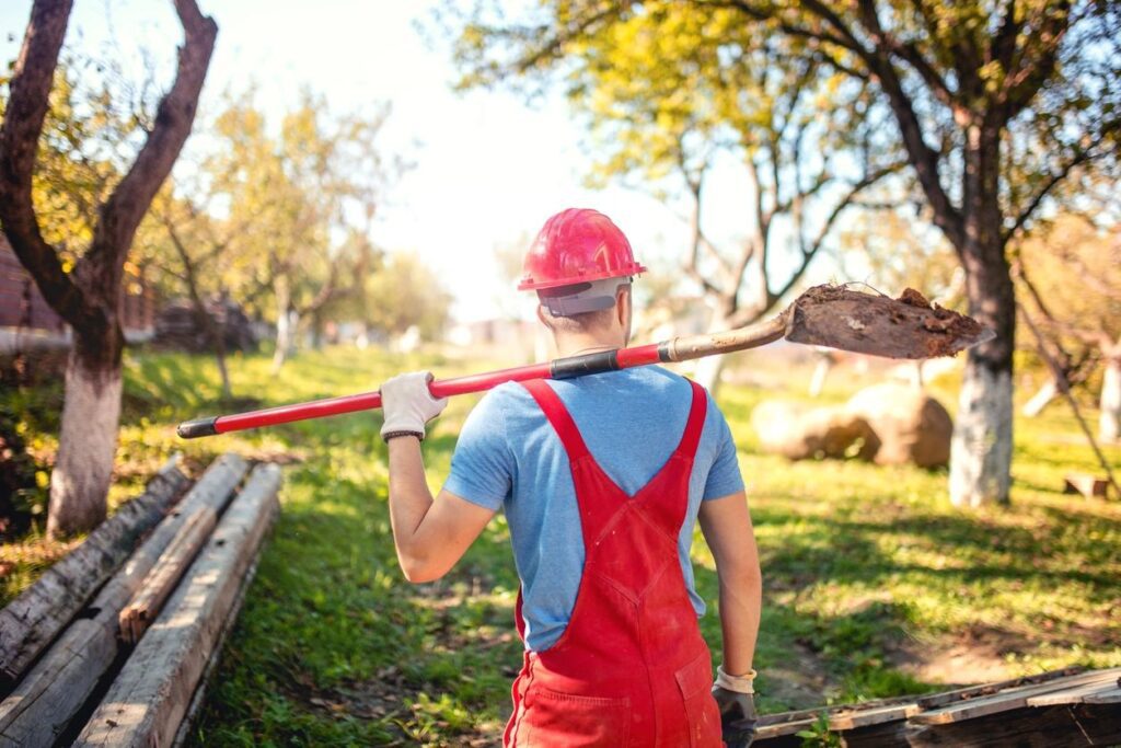 A man in red overalls holding a large wooden stick.